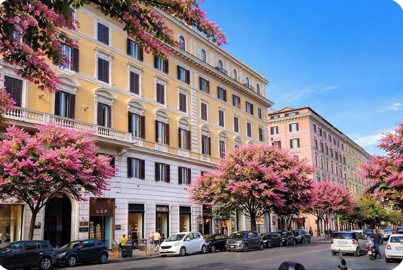 A multi-story building with balconies, storefronts, and parked cars along a street.