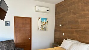 A bedroom with a wooden headboard, a bed with white linens, a patterned armchair, a door, and a wall-mounted air conditioner. - Bugambilias Hotel Hacienda (Durango)