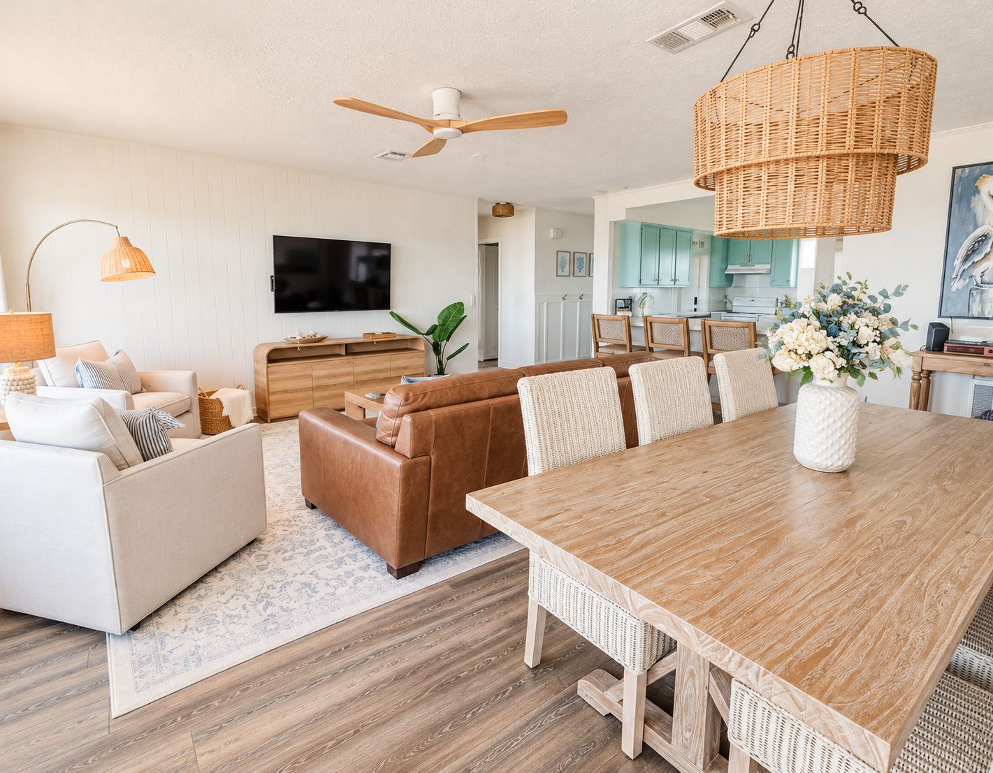 A modern living room with a wooden dining table, a brown leather sofa, and a flat-screen TV mounted on the wall.