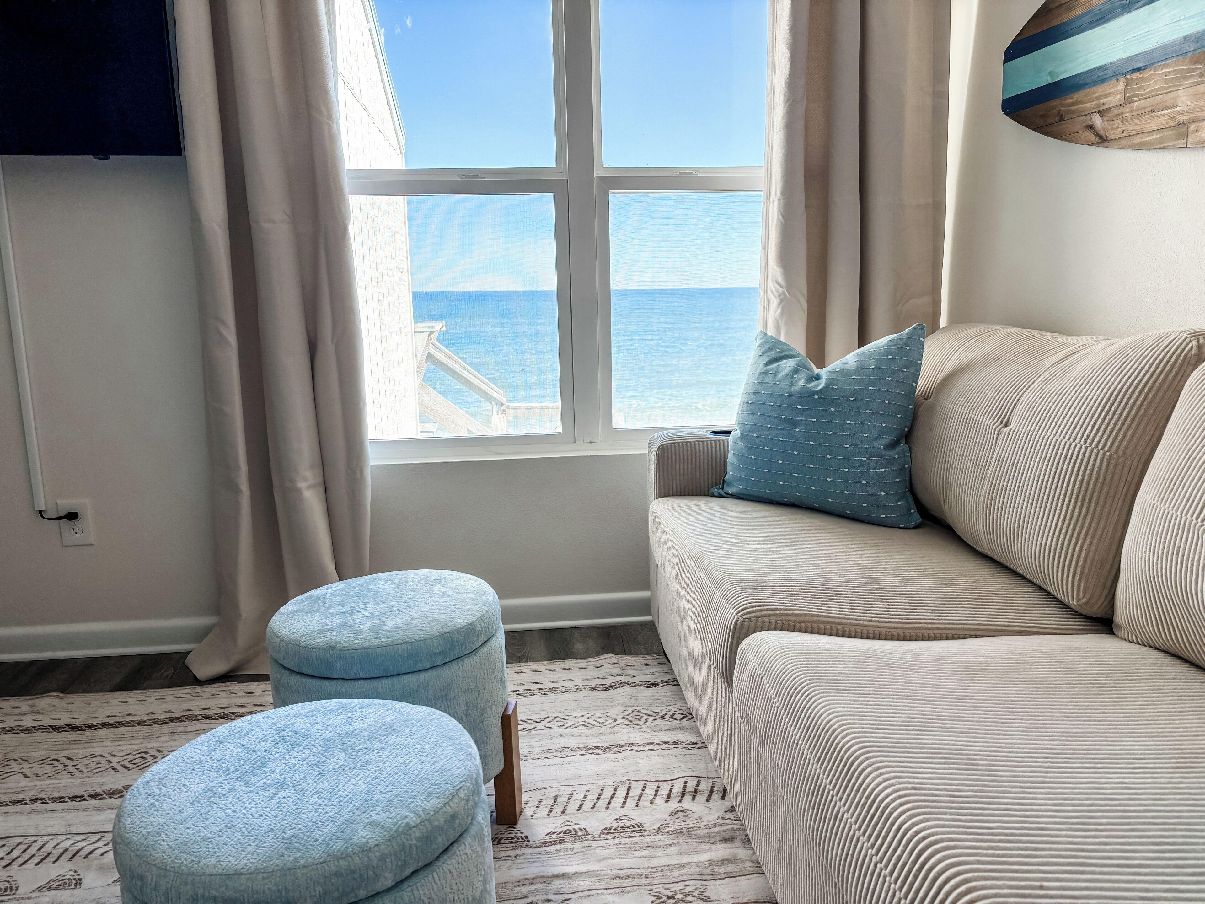 Ein Zimmer mit einem beigefarbenen Sofa, einem blauen Kissen und zwei blauen Hocker.