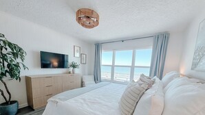 Une chambre avec un grand lit, une télévision, une plante et une vue sur la plage.