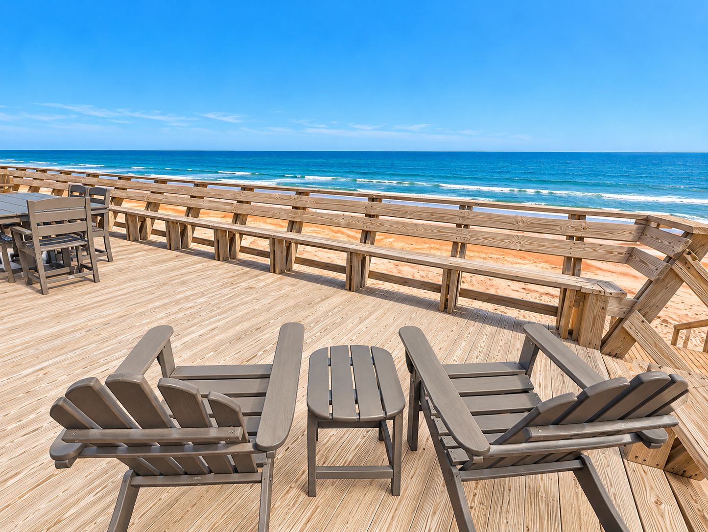 A wooden deck with seating and tables overlooking a beach.