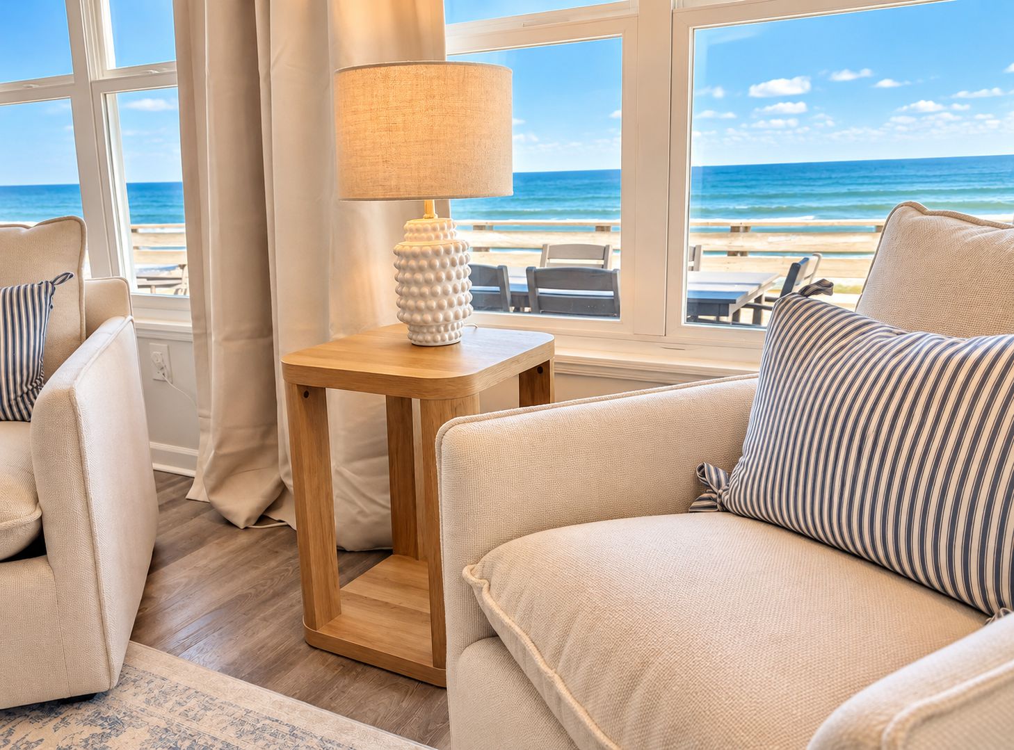 A beach view from a room with a sofa, a lamp, and a wooden side table.