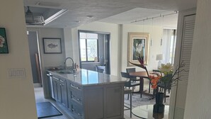 Une cuisine moderne dotée d’un îlot central, d’un coin repas avec une table en verre et d’une vue sur l’extérieur.