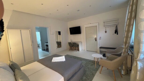 Habitación de hotel moderna con una cama grande, un escritorio pequeño, un televisor y un rincón de descanso con sillones.