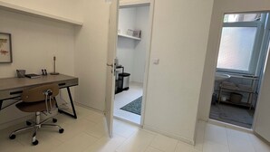 Un espacio de oficina moderno con un escritorio, una silla y estanterías. Una puerta da paso a un baño con ducha y ventana.