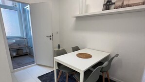 Una habitación pequeña y moderna con una mesa y sillas blancas, un tapete azul oscuro y una puerta blanca que da a otra habitación.