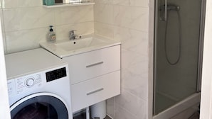 A modern bathroom with a built-in washing machine, a sink with a mirror above it, and a glass-enclosed shower. - Studio on the banks of the Seine (Rueil-Malmaison)