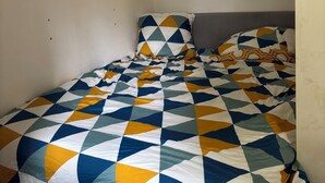 A small, single-bed room with a plain white wall and a patterned bedspread. - Studio on the banks of the Seine (Rueil-Malmaison)
