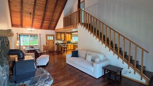 Ein geräumiger Wohnbereich mit einer Holztreppe, einem weißen Sofa und einem Steinkamin.