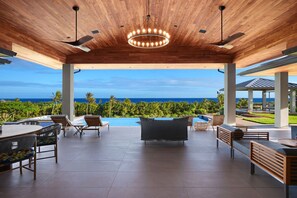 A covered outdoor area with a pool, lounge chairs, and a view of the ocean.