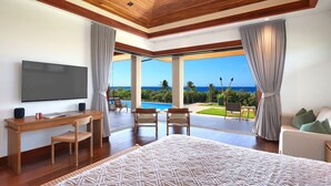 A spacious bedroom with a large bed, a desk with a TV, and a view of the ocean. - Kauai Oasis Luxe Ocean View, Pool SPA AC Sleep22 (Koloa)