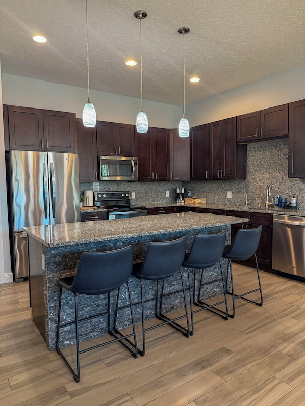 A modern kitchen with dark wood cabinets, stainless steel appliances, a granite countertop, and bar stools.