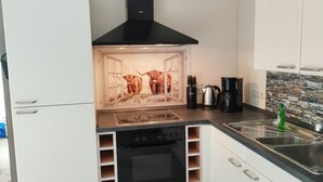 A modern kitchen with white cabinets, a black stove, and a stone backsplash. - Vacation apartment Hof Lanze with a view of the Eichenallee (Prezelle)