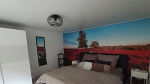 A bedroom with a large bed, a nightstand, a wall-mounted lamp, and a painting of a landscape. - Vacation apartment Hof Lanze with a view of the Eichenallee (Prezelle)