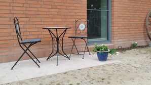 A brick building with a large window, two metal tables, and chairs, and a potted plant. - Vacation apartment Hof Lanze with a view of the Eichenallee (Prezelle)