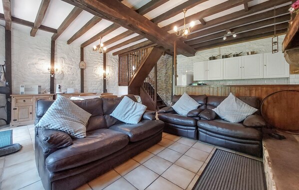 A spacious living room with a large brown leather sofa set, a wooden staircase, and a kitchen area with white cabinets. - Maison à la campagne (Le Ferré)