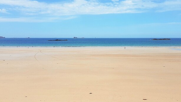 Une vaste plage de sable fin, avec une eau calme et un ciel dégagé.