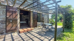 Un bâtiment en pierre avec une pergola en bois, une table et des chaises à l’extérieur.