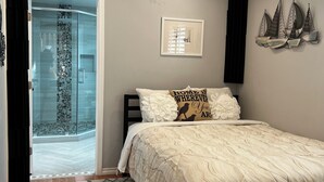 Un dormitorio con cama, ventilador de techo, ducha con puertas de vidrio y decoración náutica en la pared.
