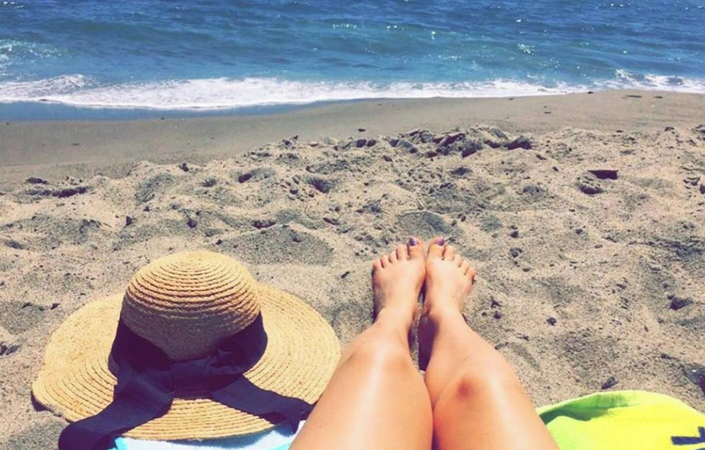 Une scène de plage avec un chapeau de paille et une serviette jaune sur le sable.