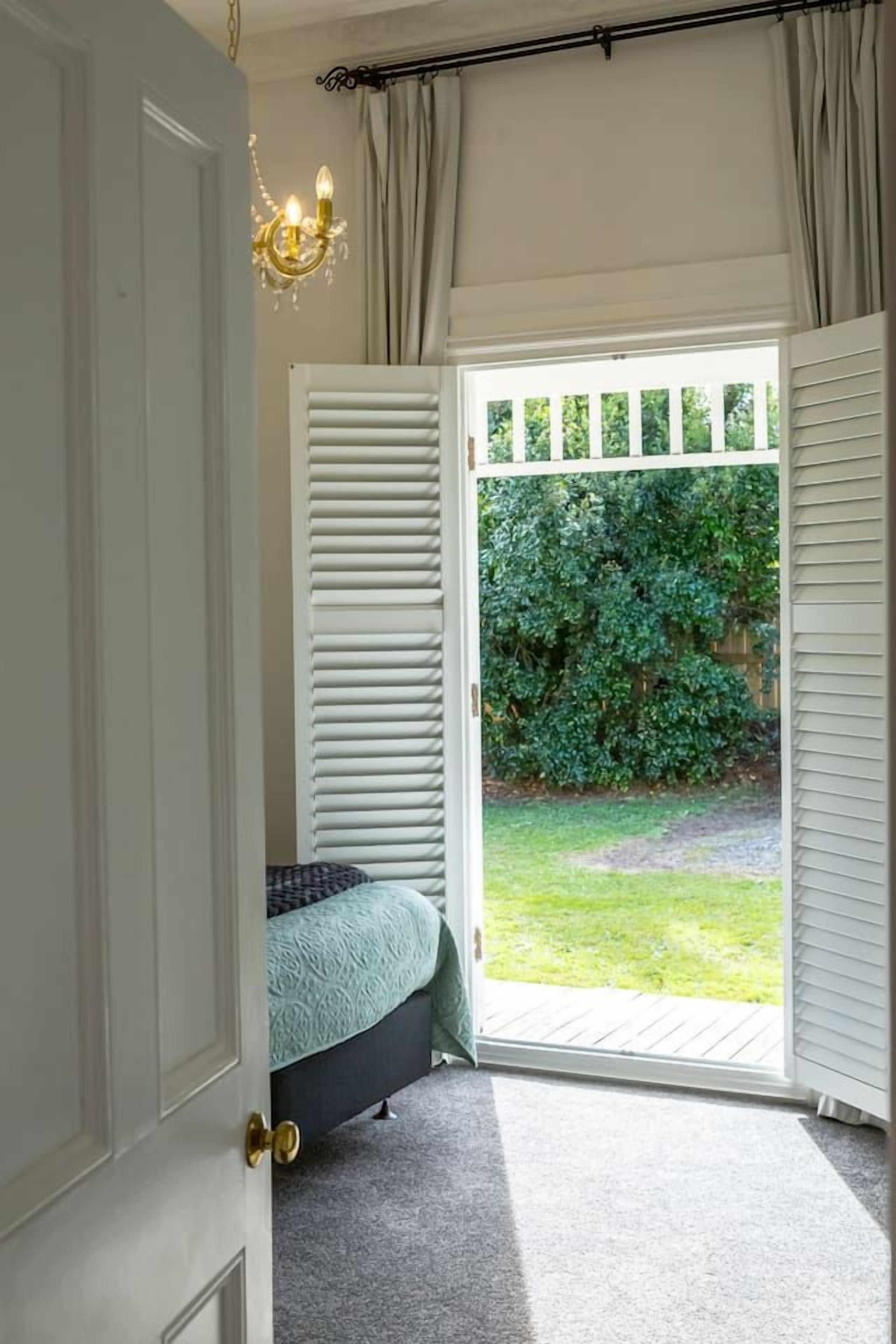 Ein Schlafzimmer mit einem Bett, einer Tür zu einem Balkon und Blick auf einen Garten.