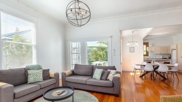 A modern living room with a grey sofa set, a coffee table, and a dining area with white chairs.
