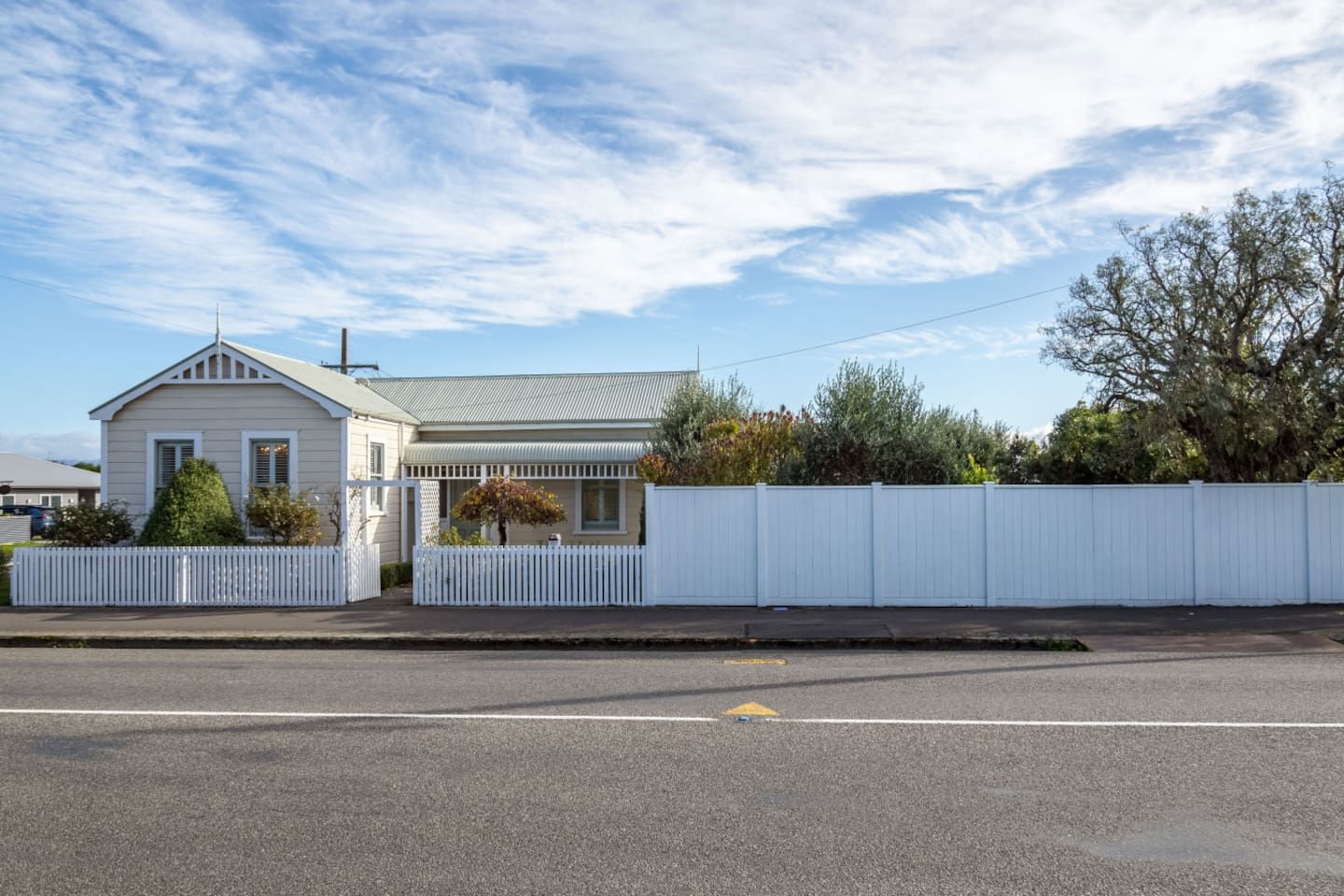 A single-story house with a gabled roof, a fenced yard, and a clear sky.