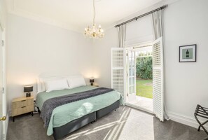 Un dormitorio con cama, lámparas de noche, una araña y una puerta que da a un jardín, además de un cuadro en la pared.