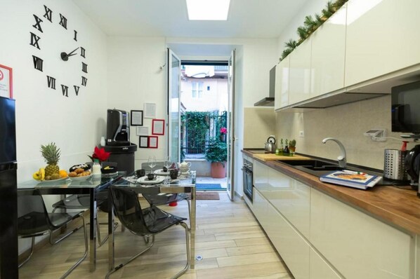 A modern kitchen with a clock on the wall, a dining area with chairs, and a view of the outside.