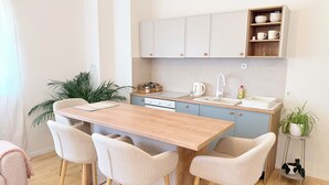 A modern kitchen with a wooden table and four chairs, a sink, cabinets, and a small shelf with dishes. - Luna Serene Garden House | Jacuzzi (Zadar)