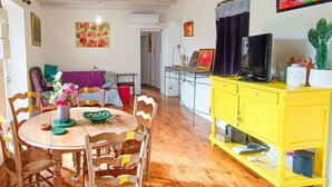A dining area with a wooden table and chairs, a yellow cabinet with a television, and a cactus plant. - Gîtes de France® - Bri-Gîte (SAINT MEDARD)