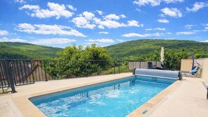 A swimming pool with a view of green hills, a covered area with a chair, and a tool case. - Gîtes de France® - Bri-Gîte (SAINT MEDARD)
