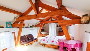 A rustic room with exposed wooden beams, a bed with floral bedding, a brown leather sofa, and a pink patterned table. - Gîtes de France® - Bri-Gîte (SAINT MEDARD)
