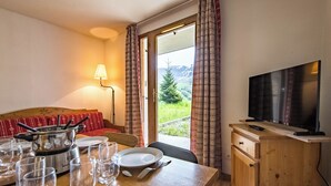 A dining area with a table set for four, a television, and a view of a mountain landscape through a window.