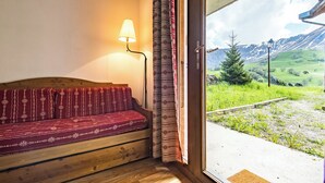 A wooden bench with patterned cushions, a wall-mounted lamp, and a view of a mountainous landscape through an open door.