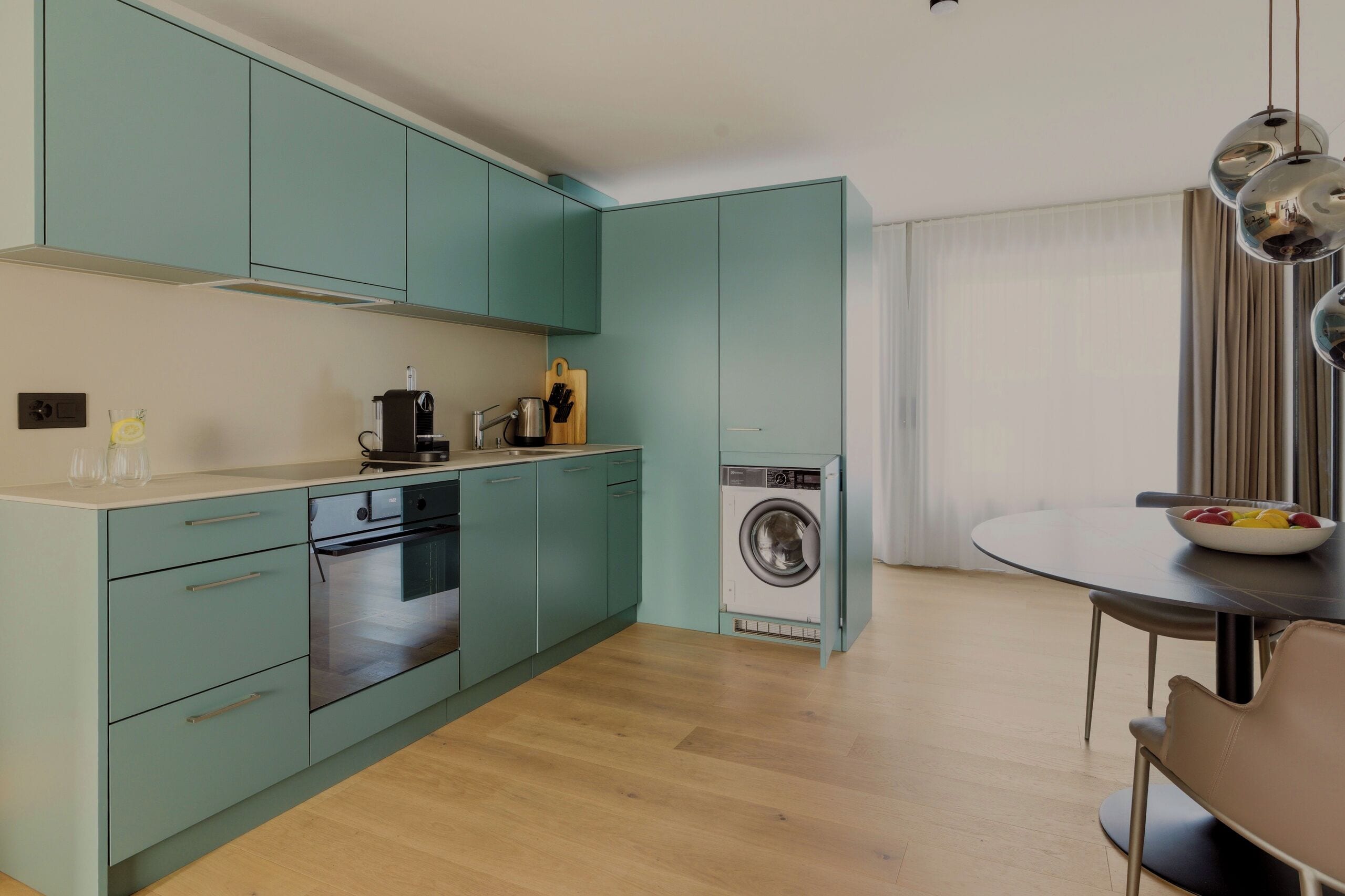 A compact kitchen with teal cabinets, a built-in oven, and a washing machine.