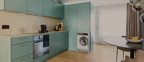 A compact kitchen with teal cabinets, a built-in oven, and a washing machine.