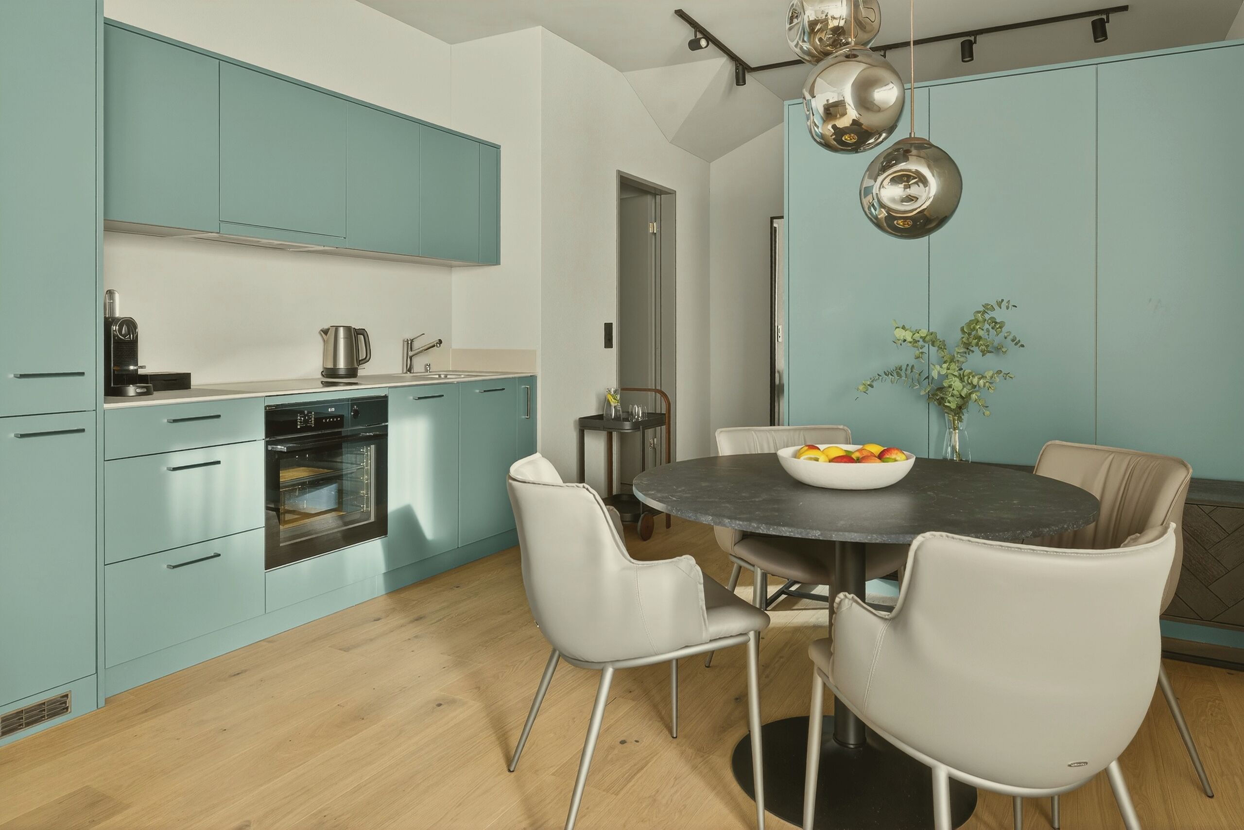 A modern kitchen with teal cabinets, a round dining table, and white chairs.