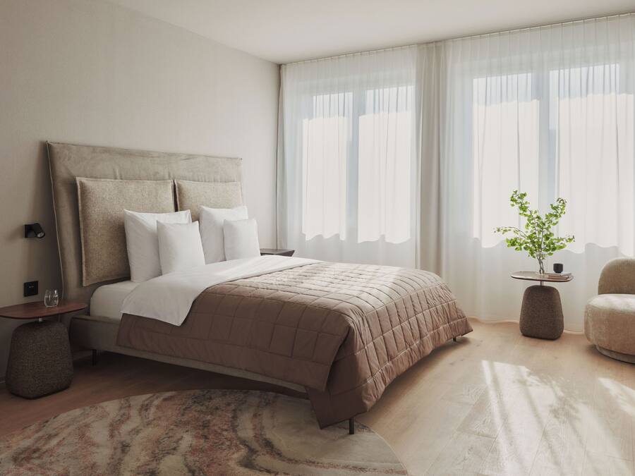 Ein modernes Schlafzimmer mit einem großen Bett, Nachttischen, einem kleinen Beistelltisch, einem Sessel und einer Topfpflanze.