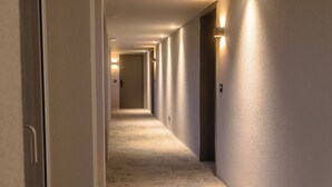 A hotel hallway with carpeted floors, light-colored walls, and doors on both sides. - Belmont Residences (Opfikon)