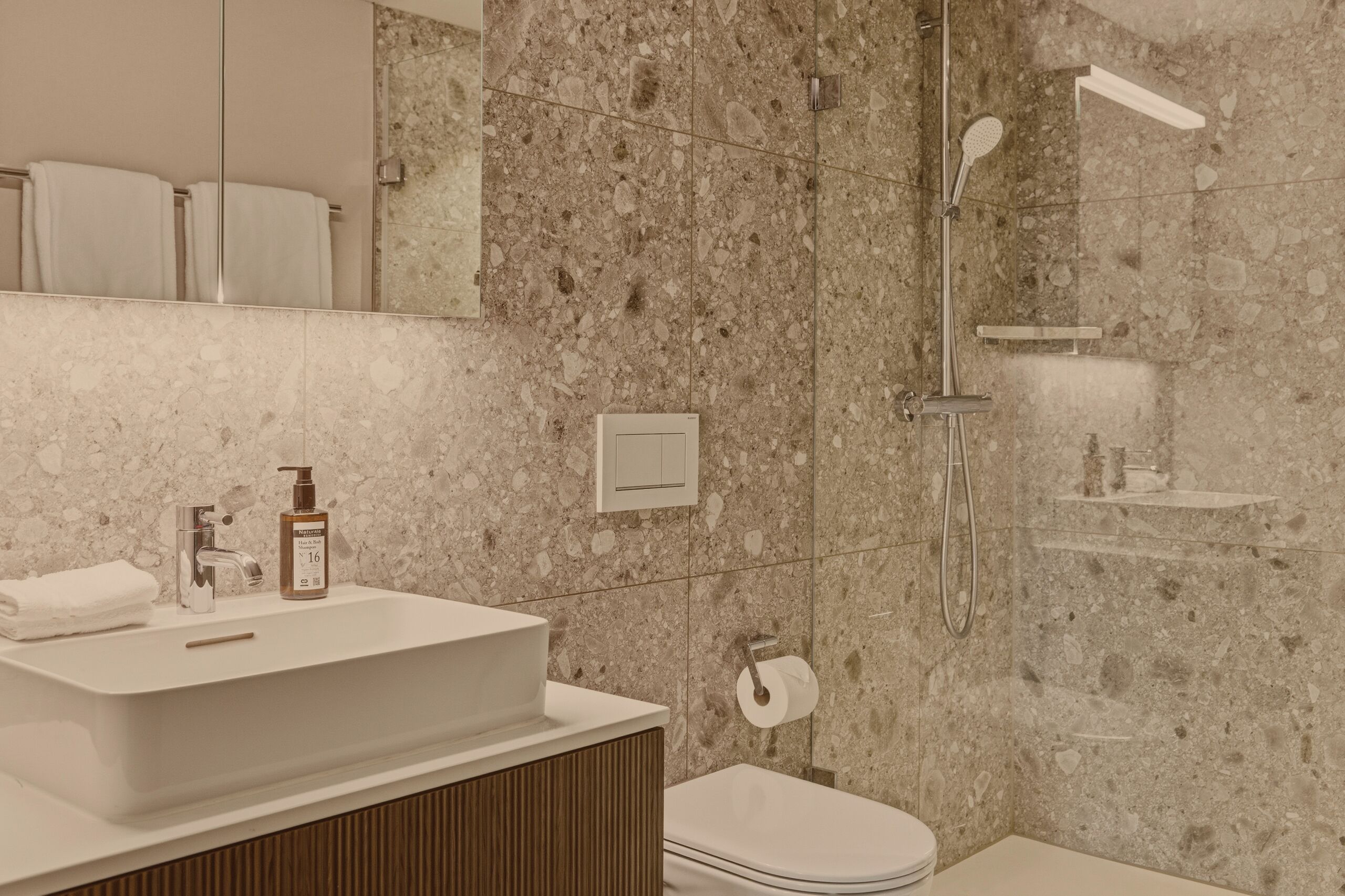 A modern bathroom with a large sink, a shower, and a toilet.