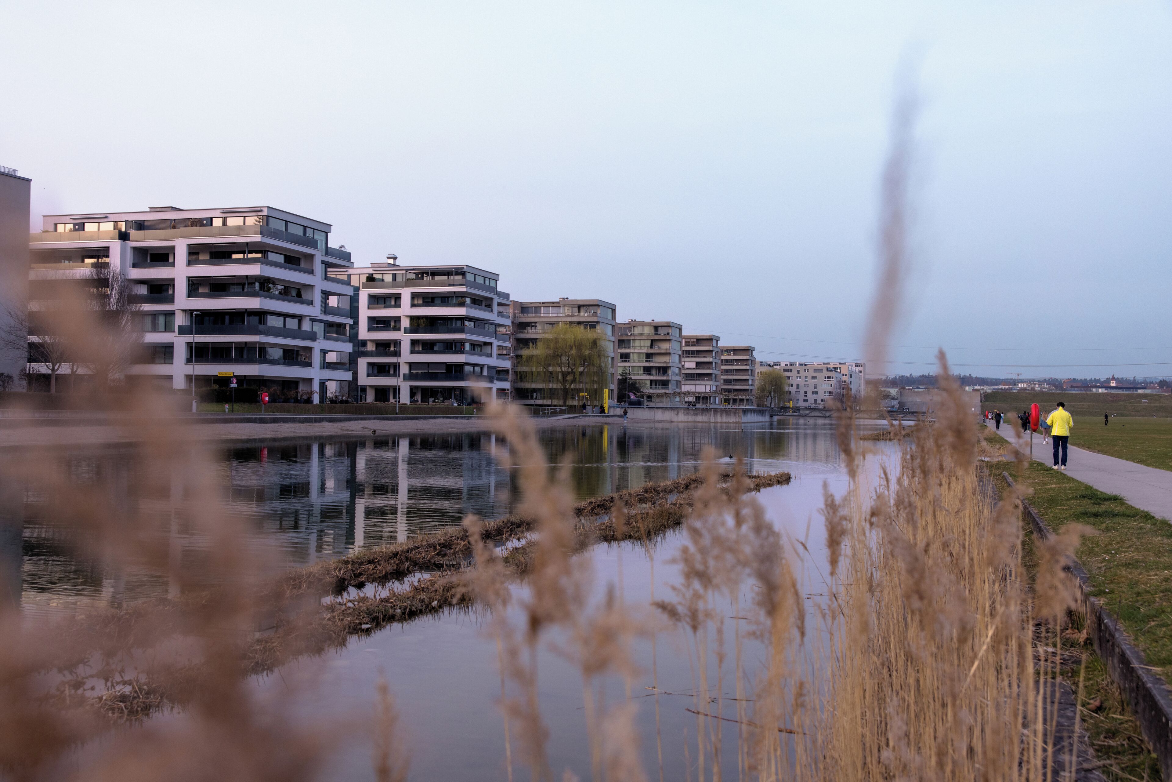 A modern building complex with multiple floors, a waterfront, and a pedestrian path.