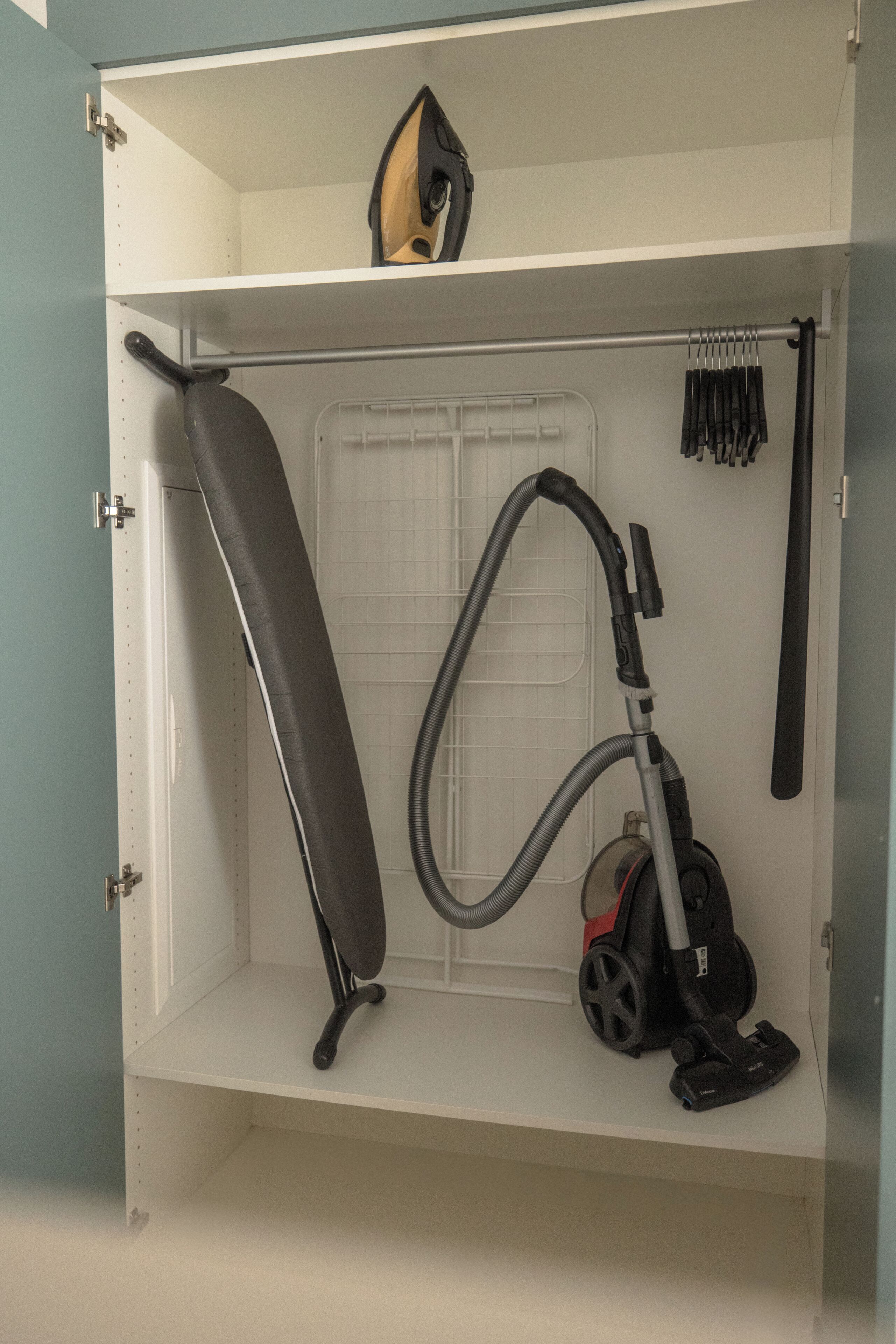 A storage unit with a vacuum cleaner, ironing board, and ironing board cover.