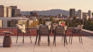 A rooftop terrace with a table set for four, surrounded by chairs, overlooking a cityscape with buildings and hills. - Belmont Residences (Opfikon)