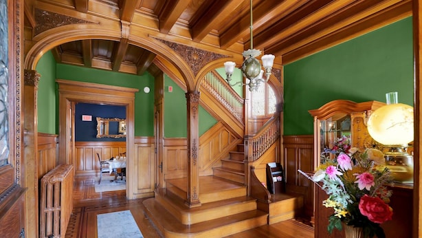 A grand staircase with ornate woodwork, a chandelier, and a floral arrangement. - Old Library Inn - Hemingway Room (Olean)
