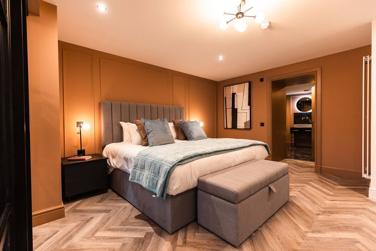 Ein modernes Schlafzimmer mit einem großen Bett, Nachttischen, einer Bank und einer Deckenleuchte.