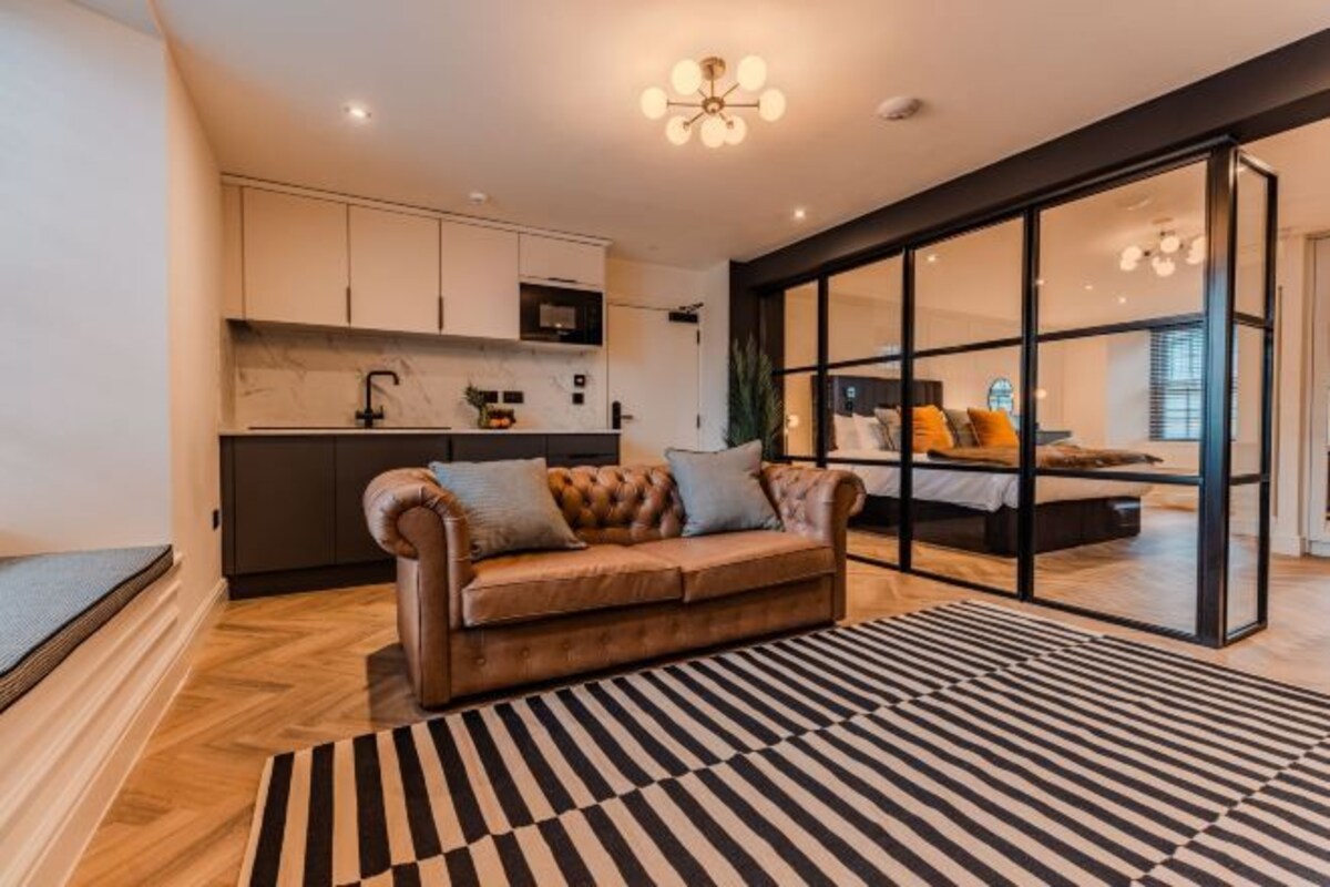 A modern living room with a sofa, a striped rug, and a kitchen in the background.