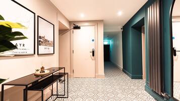 A hallway with patterned flooring, a black console table, framed pictures on the wall, and a teal-colored door.