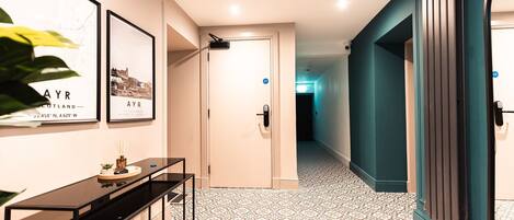 A hallway with patterned flooring, a black console table, framed pictures on the wall, and a teal-colored door.